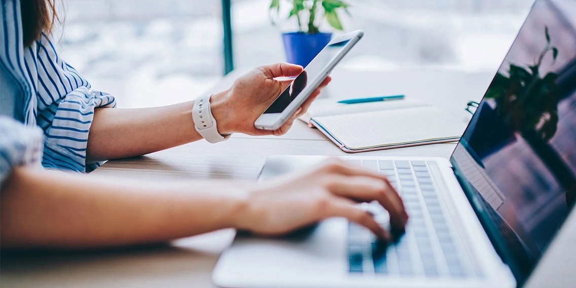 hands dialing on a smartphone and typing on a laptop