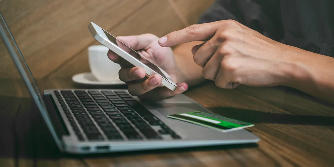 Man checking mobile infront of the laptop and using credit card