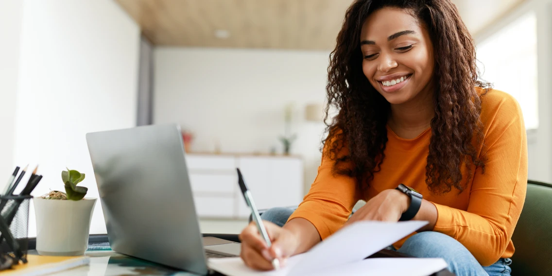 A curly hair girl writing something on a paper with a smile